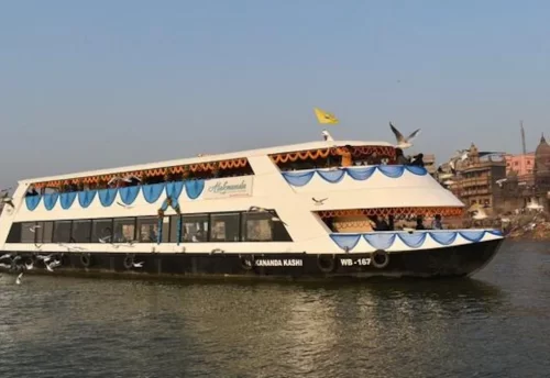 A two-deck cruise boat on the Ganga in Varanasi with the ghats behind