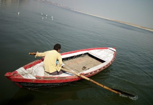 A boatman rowing a red and white wooden boat on the Ganga