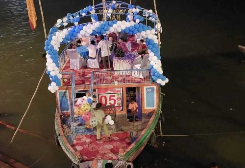 A boat decorated with flowers and balloons at a ghat in the evening