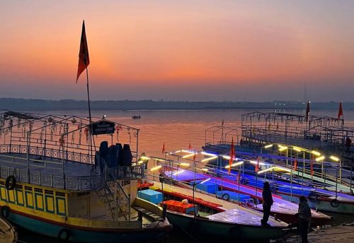 Boats with lights moored at the ghat under an orange evening sky