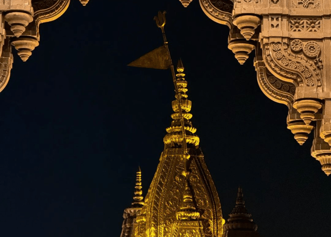 The illuminated golden spire of Kashi Vishwanath Temple framed by carved stone arches