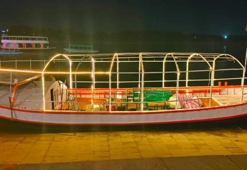 A decorated boat lit up at the ghat at night during Dev Diwali